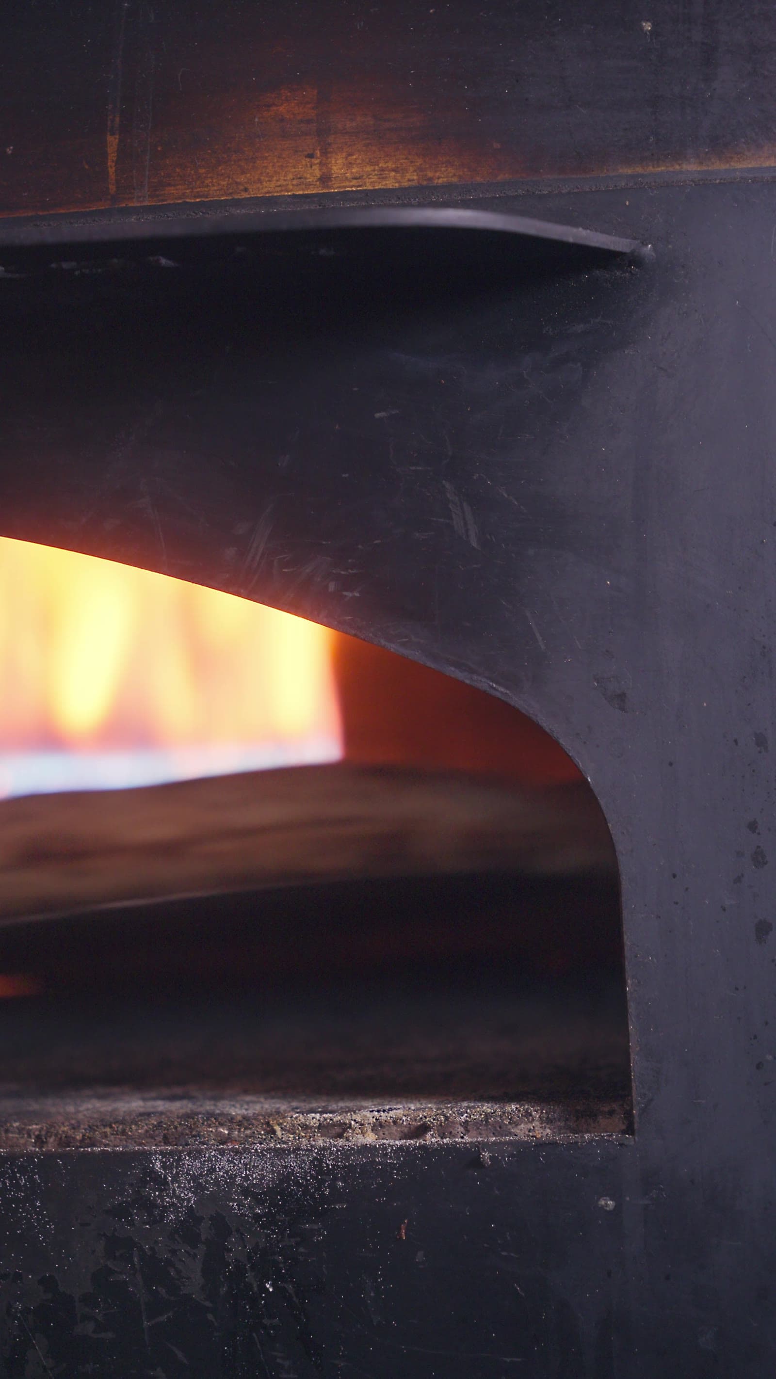 Firelight behind blackened steel, in the mouth of a wood-fired oven.