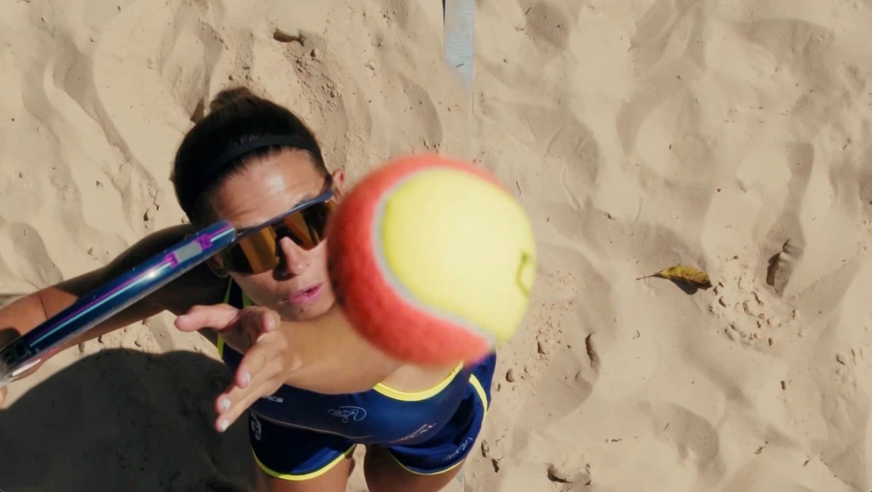 A sand court seen from above, a player set under the ball as it comes down.